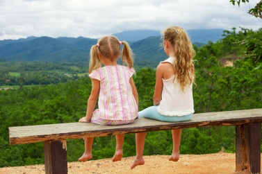 Two girls sit on the bench against the backdrop of the mountains